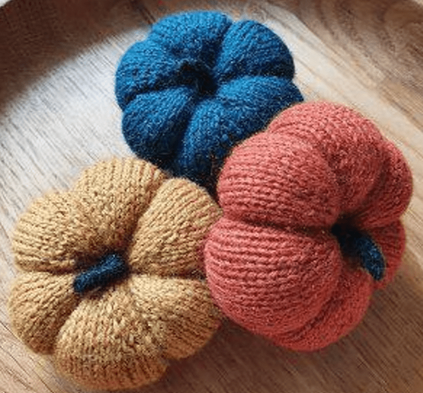 Three knitted pumpkins: yellow, orange, and blue.